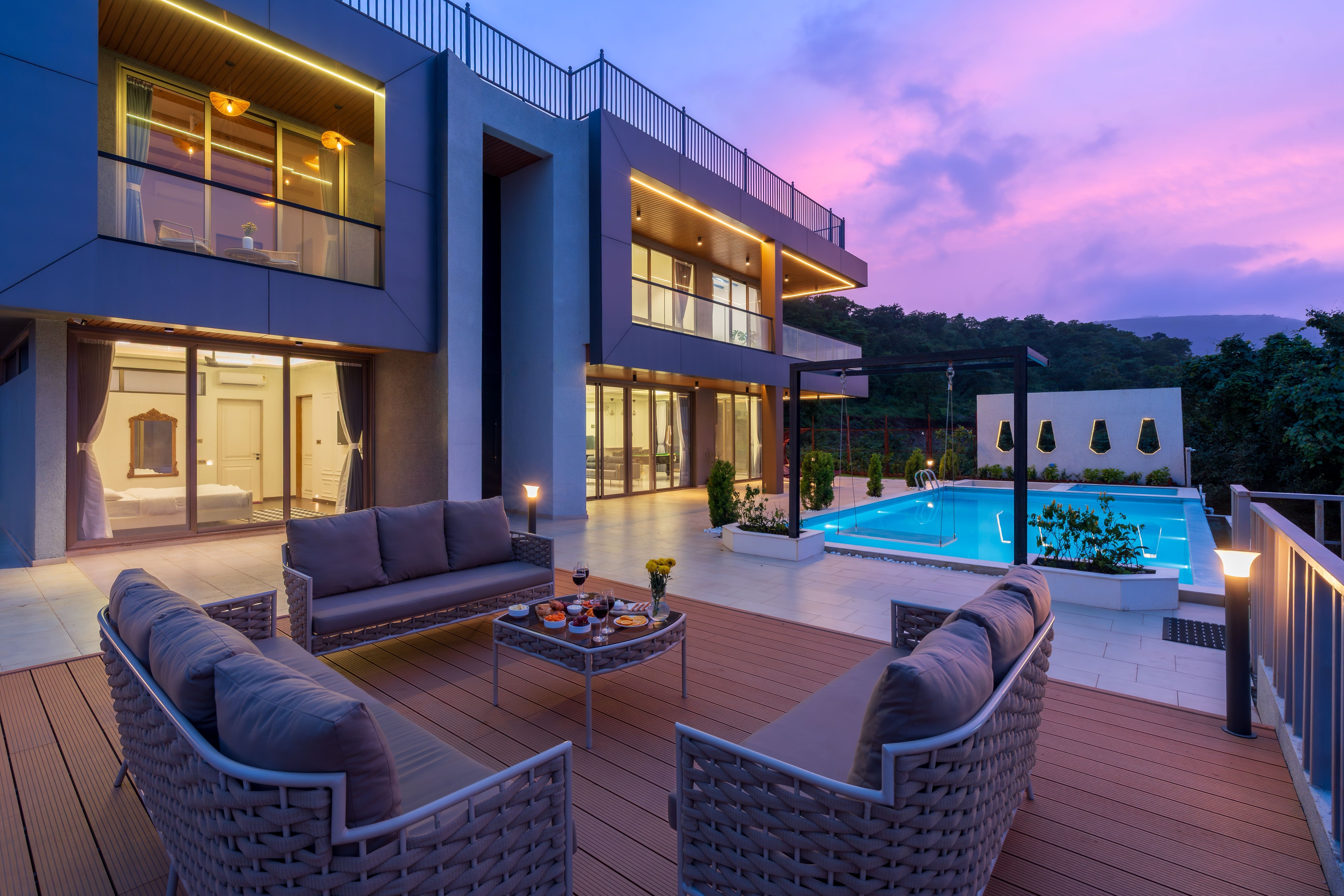 A furnished terrace and lit swimming pool at a hillside house, under a violet sunset